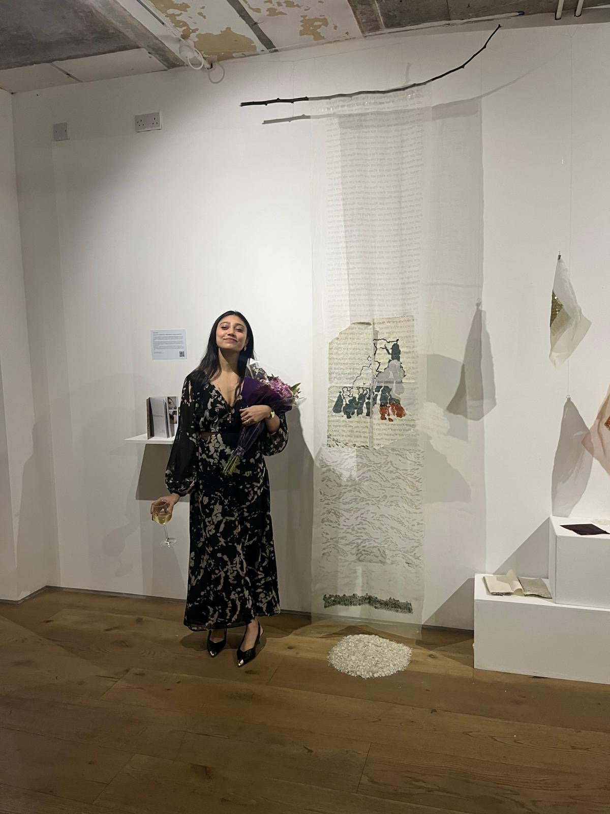Poulami Saha at the (RE)MATERIALISED opening, standing beside her hanging sequin and textile piece